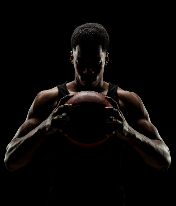A young, muscular basketball player holds a basketball in his hands.